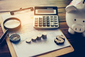 desk with various patient financial management props such as a calculator, money symbol, piggy bank, stacks of coins, and spreadsheets